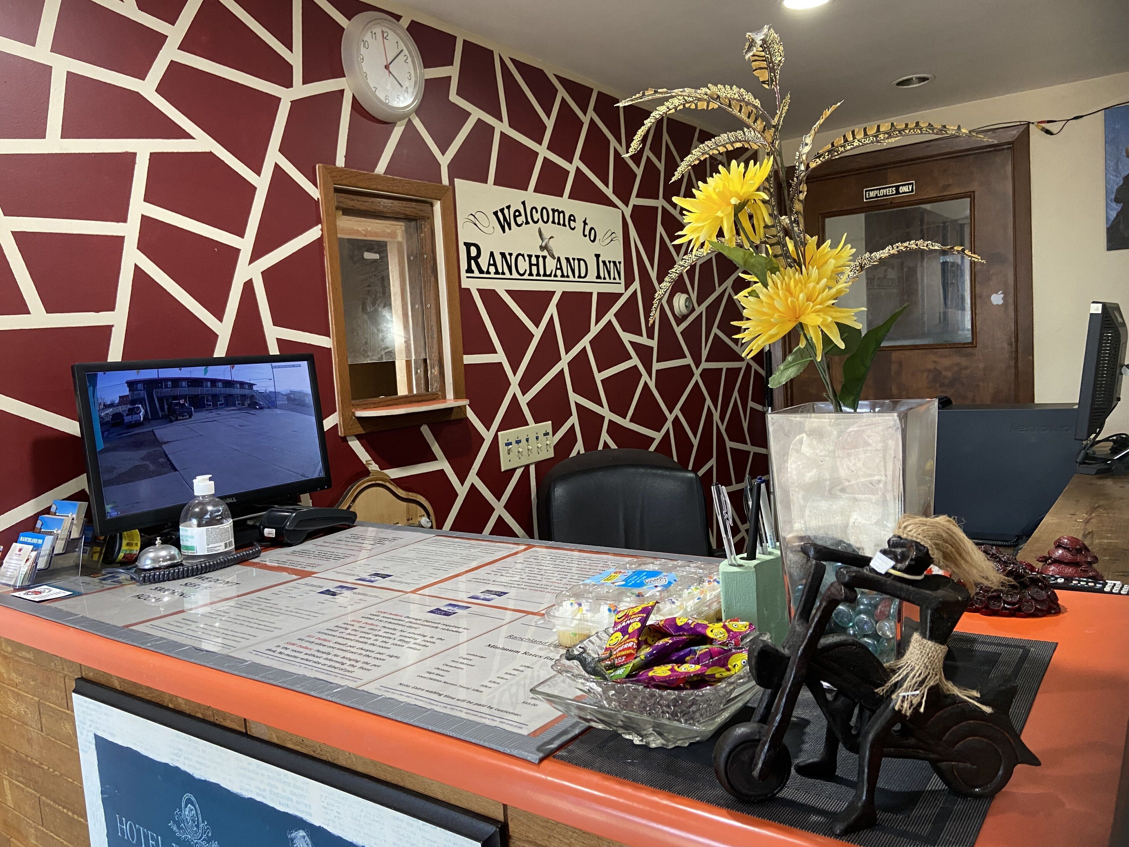 A reception desk at the Ranchland Inn with a computer monitor, a clock, and a welcome sign.