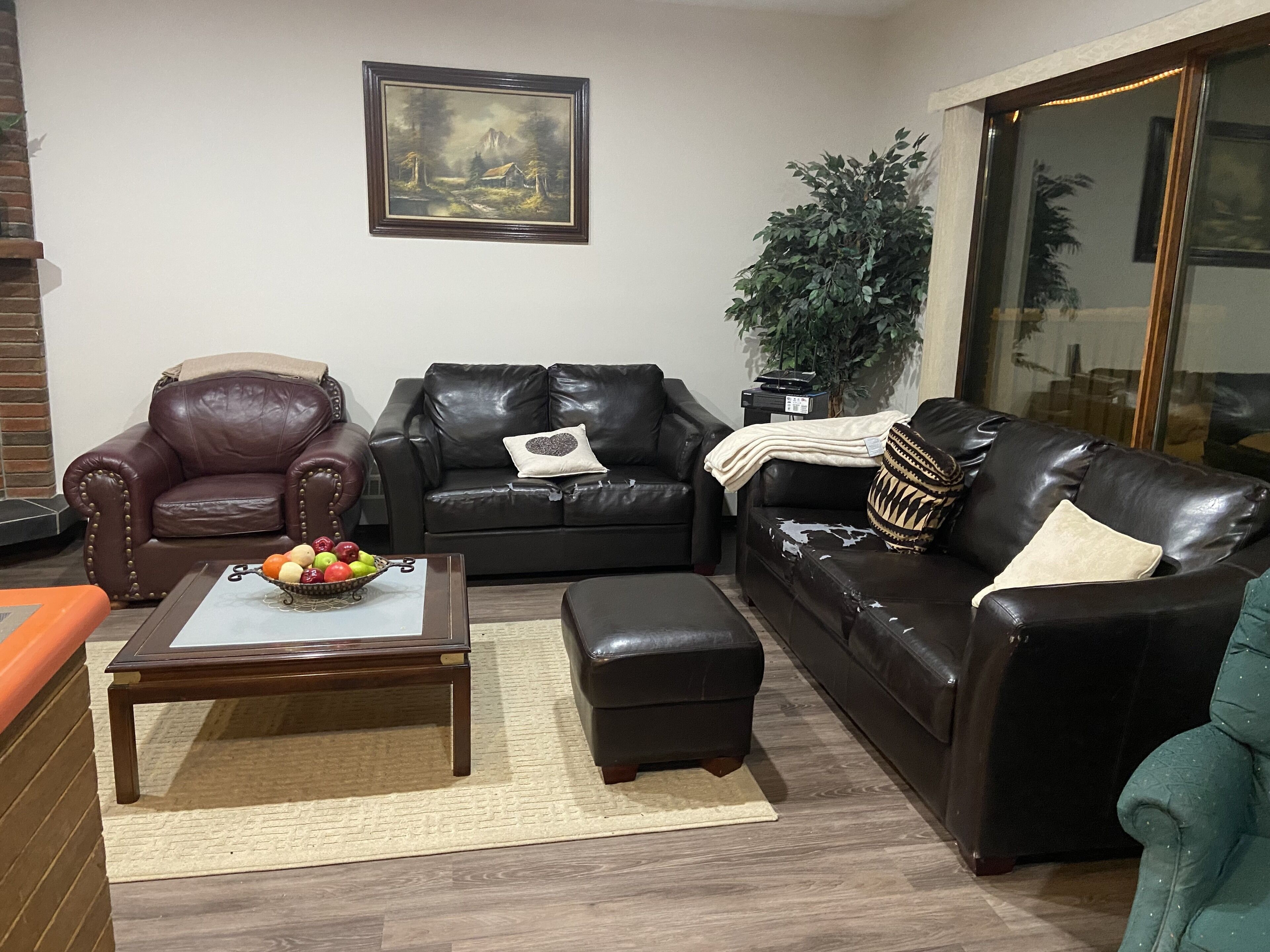 Un salón con un sillón de cuero marrón, un sofá de cuero negro, una mesa de centro de madera con fruta, y un cuadro en la pared.