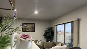 A living room with a sofa, a coffee table, a potted plant, and a painting on the wall. - Ranchland Inn (Nanton)