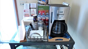 A coffee station with a coffee maker, cups, and a basket of utensils on a table. - Ranchland Inn (Nanton)