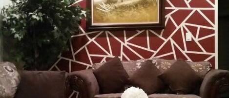 A living room with a patterned wall, a sofa, a coffee table, and a large plant.