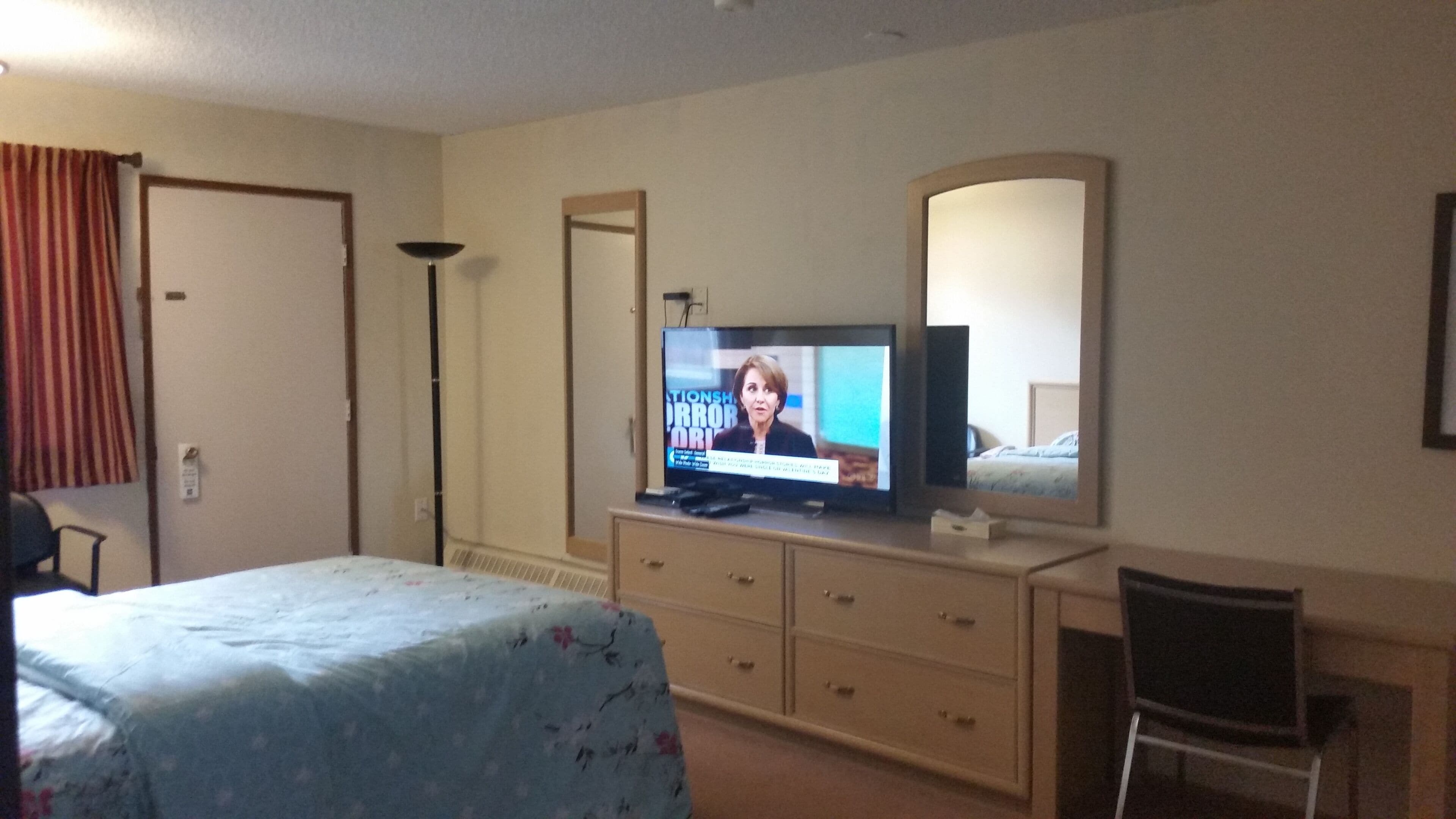 Una habitación de hotel con una cama, televisión, cómoda, silla y espejo.