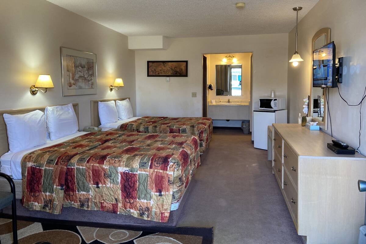 A hotel room with two beds, a desk, a mirror, a television, and a bathroom.
