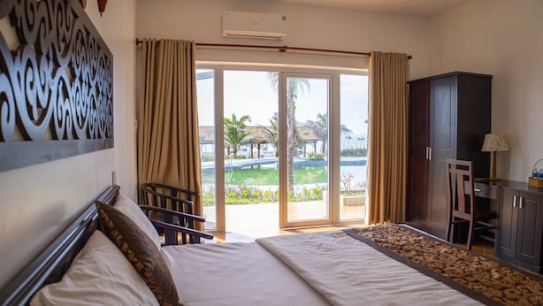 Ein Hotelzimmer mit einem großen Bett, einem Schreibtisch, einem Sessel und Blick auf einen Pool und Palmen.