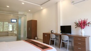 A modern bedroom with a large bed, a desk with a chair, a television, and a bathroom with a shower and a toilet.