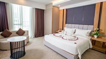 Habitación de hotel con una cama grande, un sofá, una pequeña mesa redonda y una mesita de noche con lámpara.