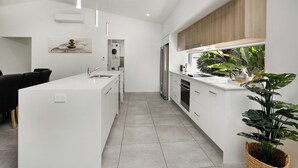 A modern kitchen with white cabinetry, a central island, stainless steel appliances, and a large window with natural light. - Heated pool Seaside at Palm cove (Cairns)