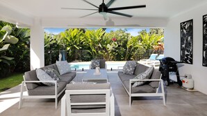 A modern outdoor living area with a pool, grey and white furniture, and tropical plants. - Heated pool Seaside at Palm cove (Cairns)