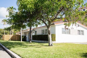 A single-story house with a white exterior, a brick foundation, and a small front yard with a tree.