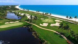 Campo de golf con vista al mar, palmeras y un cuerpo de agua.