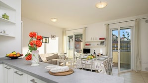 A modern kitchen with a dining area, a TV, and a balcony with a view.