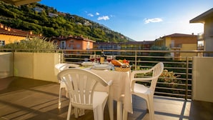 A terrace with a table set for dining, chairs, and a view of a hillside with buildings.