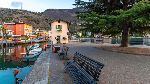 A waterfront promenade with benches, a small building, and boats docked by the water.