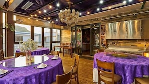 A restaurant with round tables covered in purple tablecloths, a chandelier, and a view of the sea through large windows. - BBQ Hostel Ha Long (Ha Long)