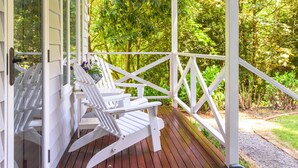 Una terraza de madera con sillas Adirondack blancas y un ventanal.