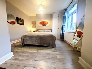 A bedroom with a bed, a bedside table, a mirror, and a window with curtains. - Beautiful 4 bed 2 bath home in central location with back garden (London)