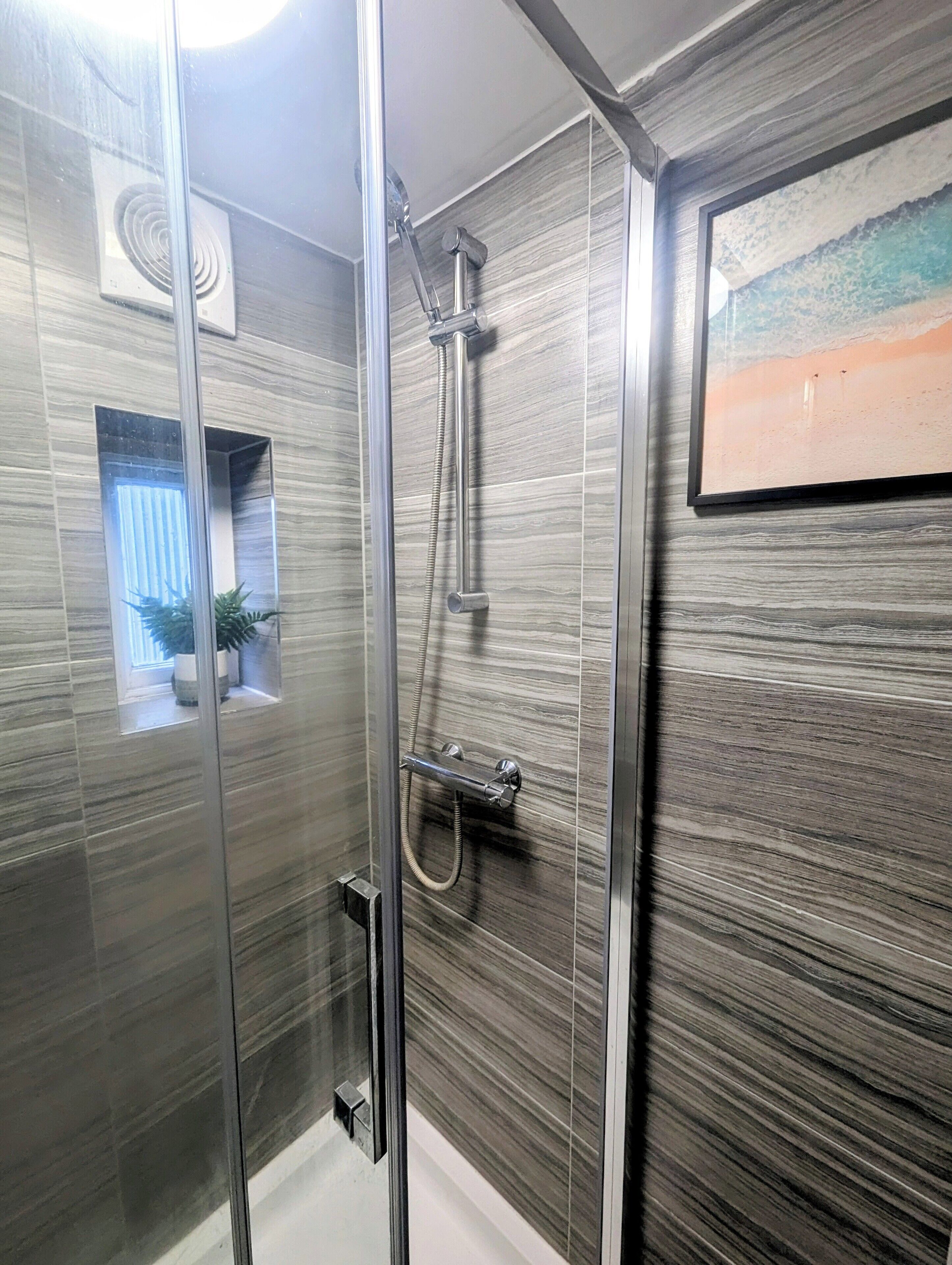 A modern bathroom with a glass shower enclosure, a potted plant, and a framed artwork on the wall.