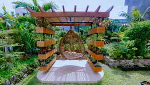 Un jardin agrémenté d’une pergola en bois, de fauteuils suspendus et de différentes plantes en pot.
