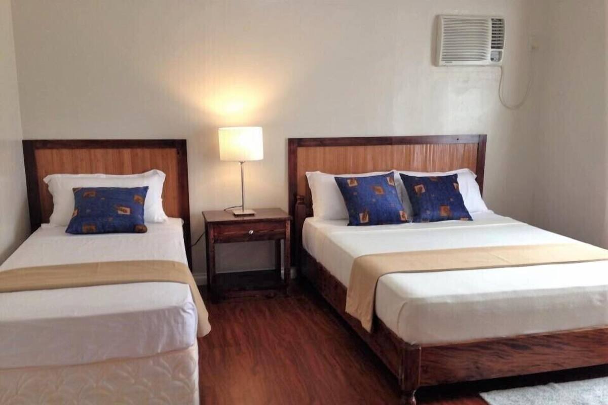 Habitación de hotel con dos camas, una mesita de noche, una lámpara y un aire acondicionado.