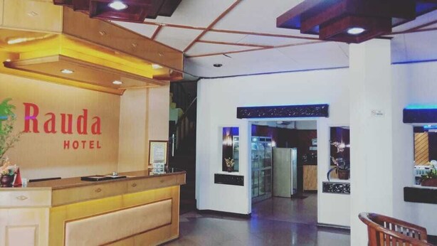 A hotel reception area with a wooden reception desk, a sign reading "Rauda Hotel", and a modern interior design. - Rauda Hotel Syariah (Pekanbaru)