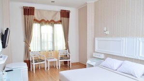 A hotel room with a bed, two chairs, a desk, a small table, and a TV. - Rauda Hotel Syariah (Pekanbaru)