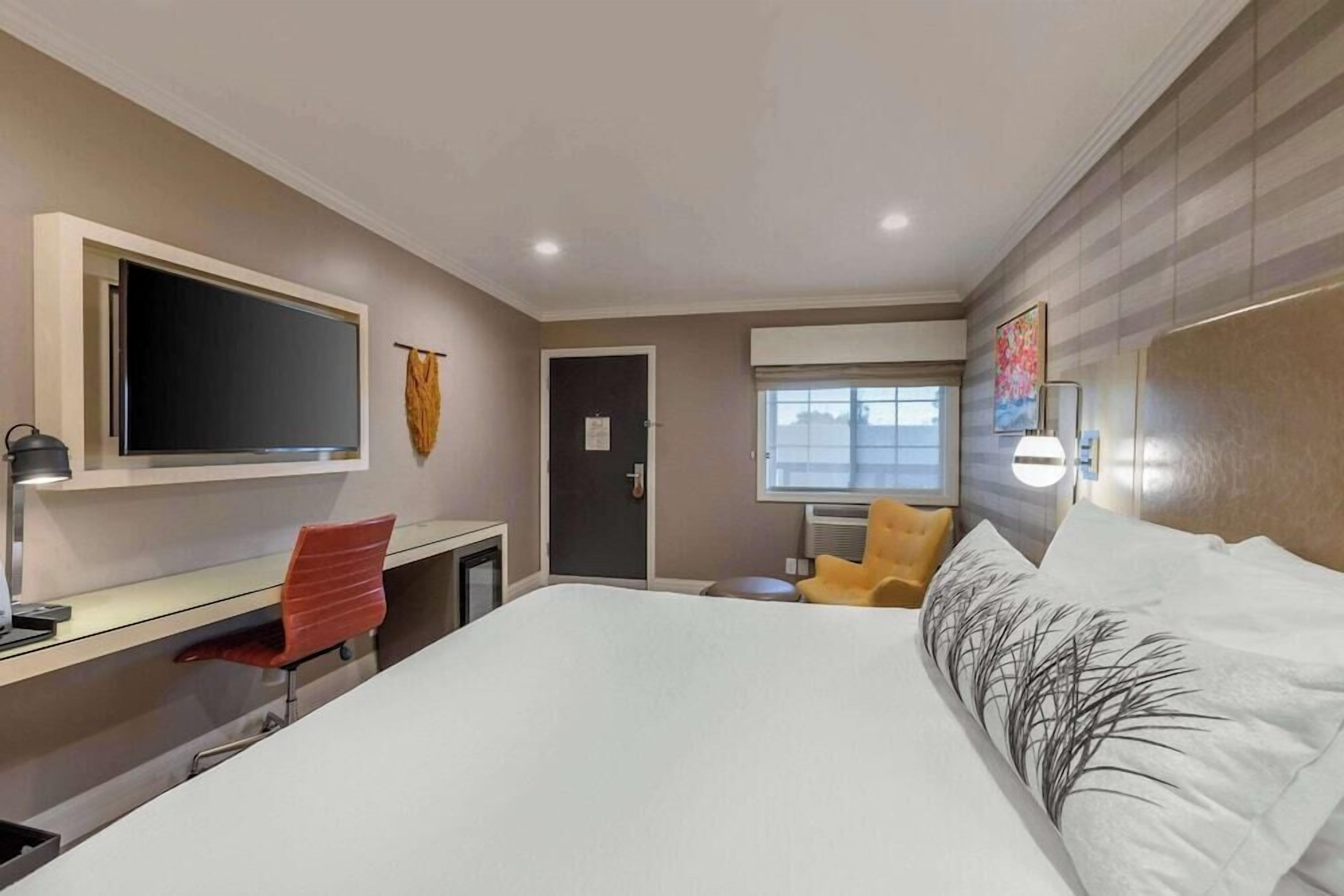 A hotel room with a bed, a desk, a chair, a TV, a window, and a door.