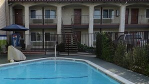 A swimming pool with a metal ladder, surrounded by a fence and a building with multiple windows and a covered area. - Bluestem Hotel Torrance Los Angeles, an Ascend Collection Hotel (Torrance)
