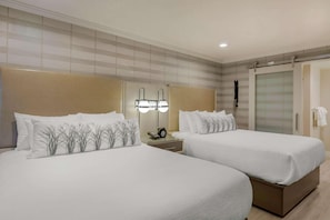 Two single beds with white bedding and decorative pillows, each flanked by a nightstand with a lamp and a telephone.