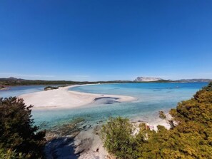 Et kystlandskab med klart vand, en sandstrand og et bjergrigt baggrund.