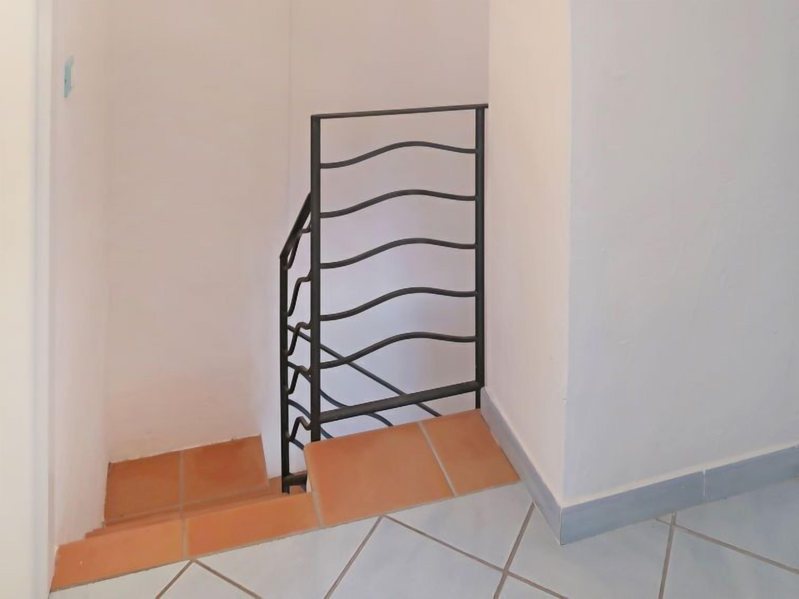 A staircase with a metal railing and orange-tiled steps.