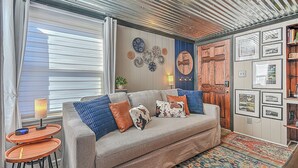 A cozy living room with a grey sofa, blue and brown cushions, a patterned rug, and a wooden door. - The View Finder at Tannery Flats - Newly Renovated! (Johnson City)