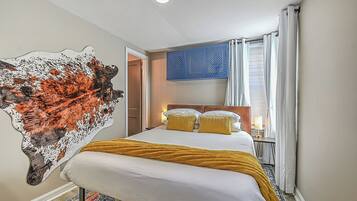 A hotel room with a large bed, a decorative wall piece, a window with curtains, and a nightstand with a lamp.