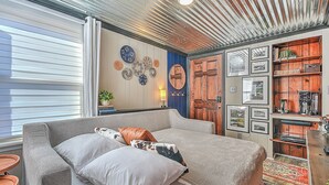 A cozy living room with a large grey sofa, a coffee table, and a wooden bookshelf with various items. - The View Finder at Tannery Flats - Newly Renovated! (Johnson City)