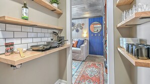 A kitchen with wooden shelves, a countertop, and a dining area with a blue wall and a mirror. - The View Finder at Tannery Flats - Newly Renovated! (Johnson City)
