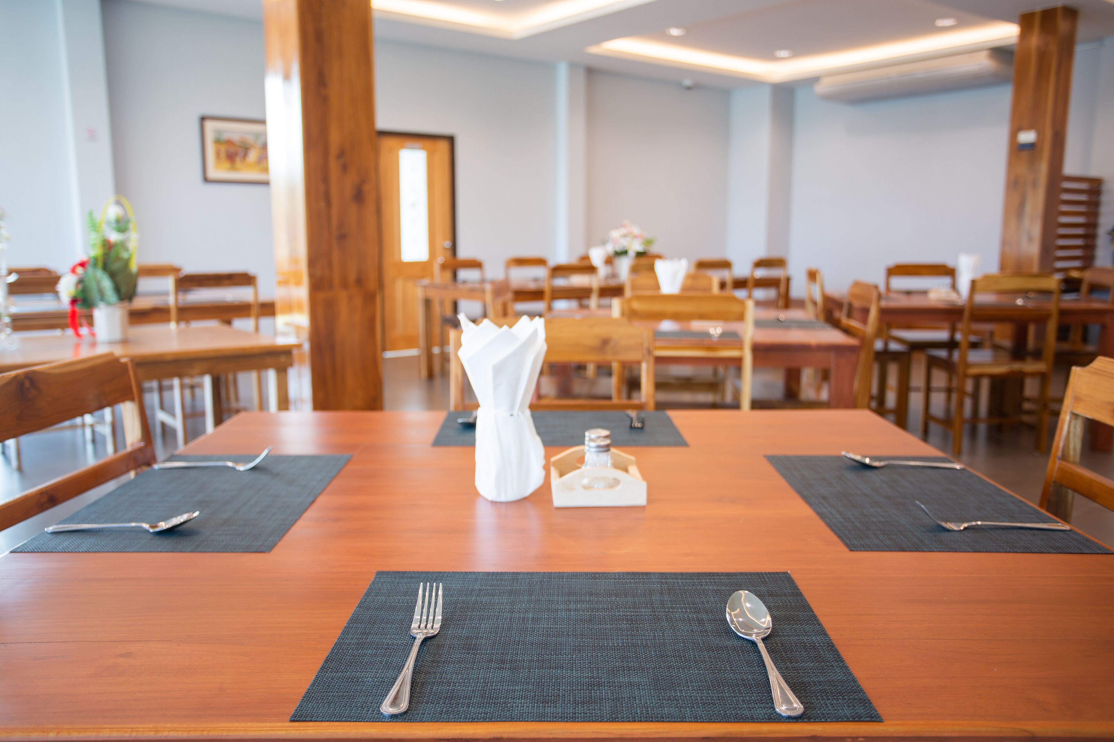 Un comedor con mesas y sillas de madera, manteles individuales negros y cubiertos plateados.