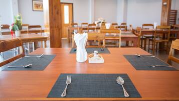 Un comedor con mesas y sillas de madera, manteles individuales negros y cubiertos plateados.
