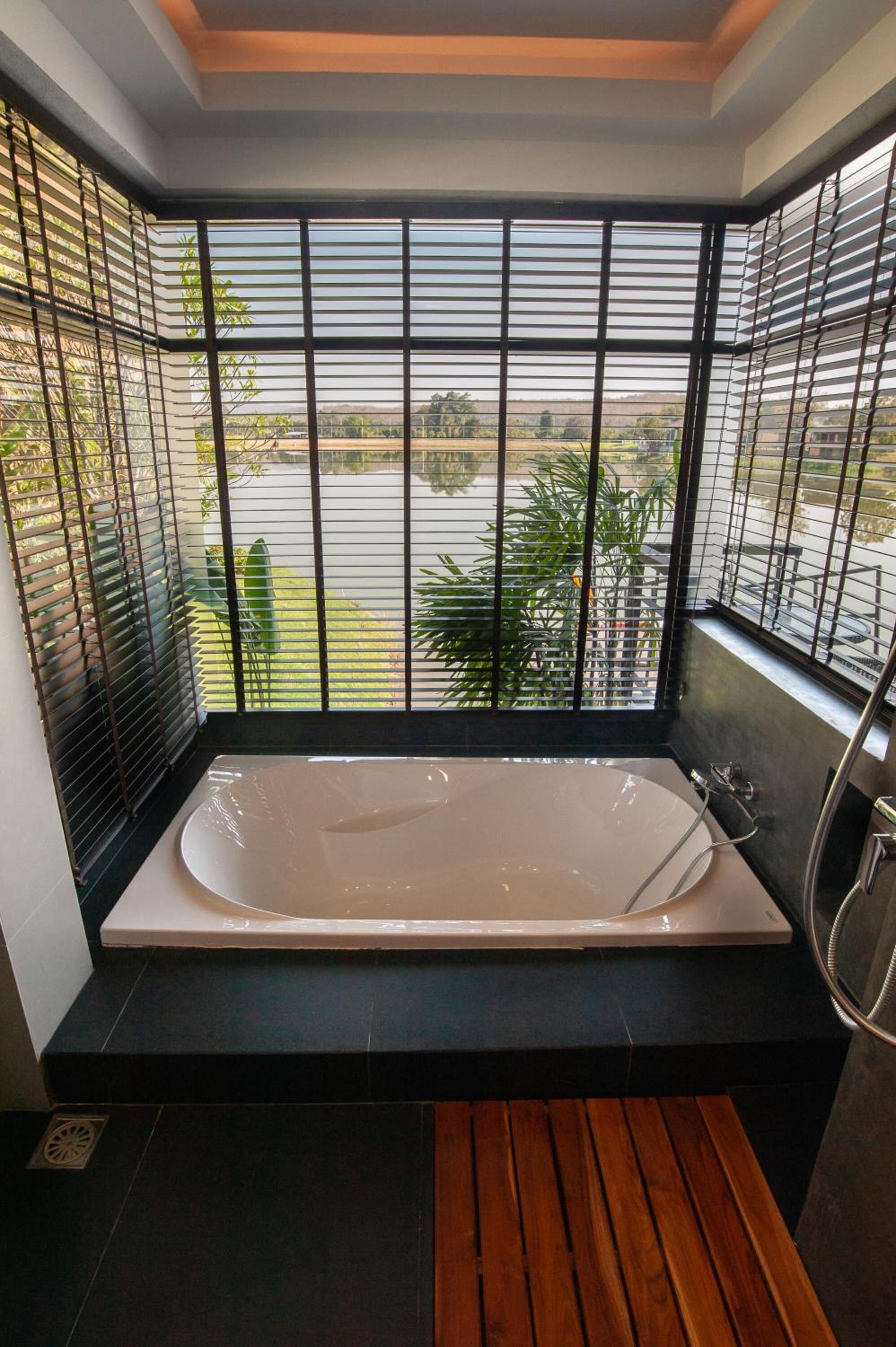 A modern bathroom with a large bathtub, black tiled walls, and a view of a river through metal bars.