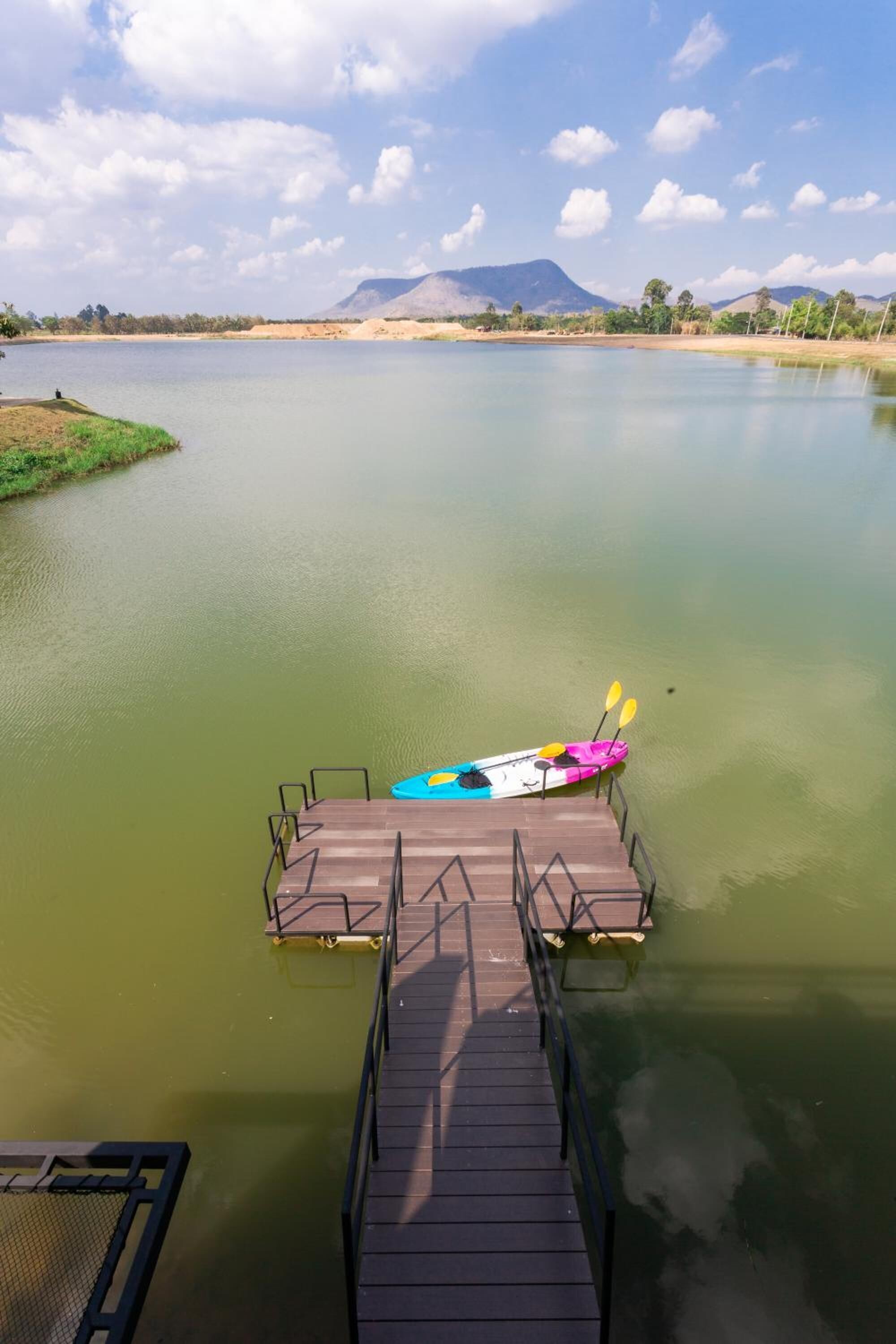 A wooden dock extending into a calm lake with a kayak and paddleboard on it.