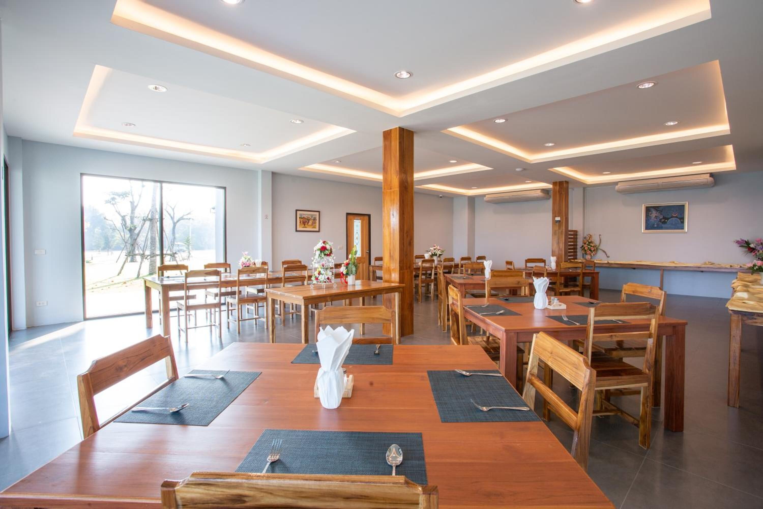Un comedor amplio con mesas y sillas de madera, iluminación empotrada en el techo y ventanas grandes que dejan entrar luz natural.