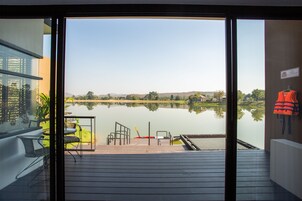 Vista desde un balcón con terraza de madera que da a un lago tranquilo, una silla y un chaleco salvavidas colgado en la pared.