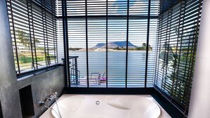 Une salle de bain moderne avec une grande baignoire, une vue sur un plan d’eau et une montagne en arrière-plan.
