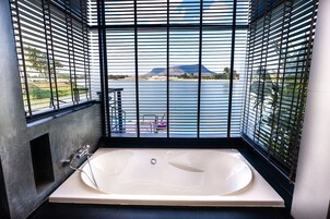 Un baño moderno con una bañera grande, vista a un cuerpo de agua y una montaña al fondo.