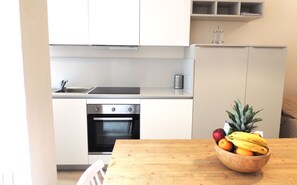 Eine moderne Küche mit weißen Schränken, einem Edelstahlbackofen und einem Holzespeisetisch mit Obstschale.