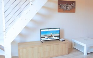 Ein modernes Wohnzimmer mit einem Holzschrank, einem Fernseher, der eine Strandansicht zeigt, und einem hölzernen Wandbild.