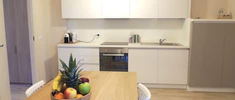 A modern kitchen with white cabinets, a wooden dining table with a fruit bowl, and a built-in dishwasher.