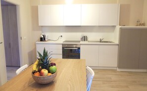 Eine moderne Küche mit weißen Schränken, einem Holztisch mit Obstschale und einem integriertem Geschirrspüler.