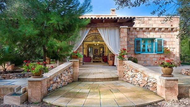 Un bâtiment en pierre avec une entrée carrelée, des plantes en pot et une vue sur l’intérieur.