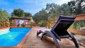 Une terrasse en bois avec une piscine, une chaise longue et un bâtiment rustique en arrière-plan.