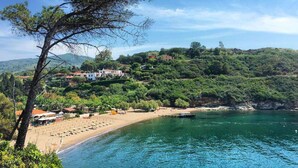 A coastal area with a beach, a pier, and buildings on a hillside.
