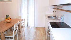 A modern kitchen with white cabinetry, a wooden dining table, and a fruit bowl.